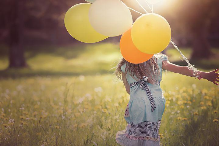 Girl running in a filed with balloons.